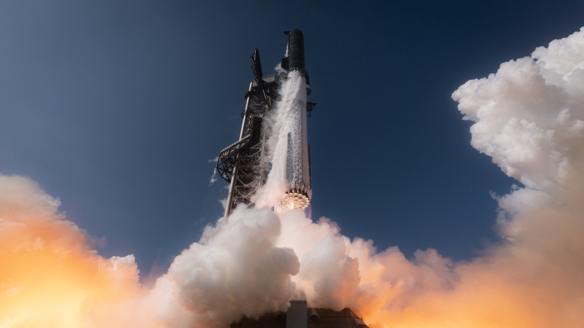 A towering SpaceX Starship Flight 12 rocket lifts off into a blue sky belching twin plumes of smoke