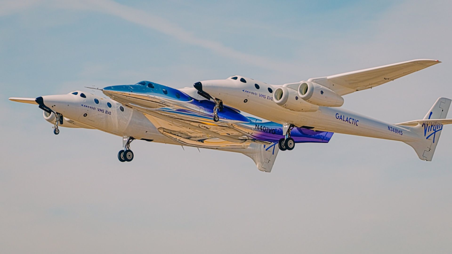 closeup of a space plane in flight, being hauled beneath the wings of a white, two-fuselage carrier aircraft