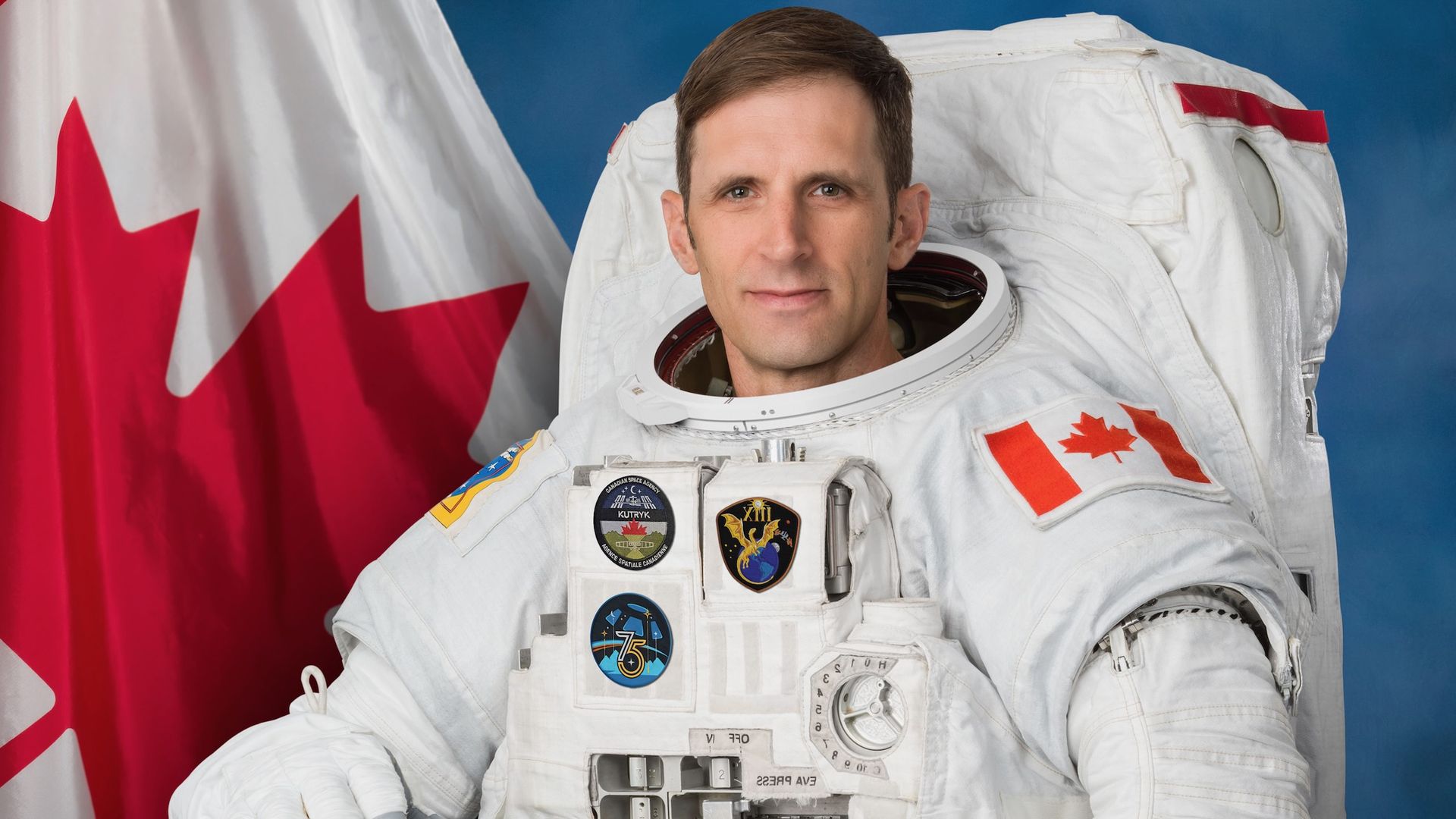 official portrait of an astronaut in a white spacesuit, with the canadian flag in the background