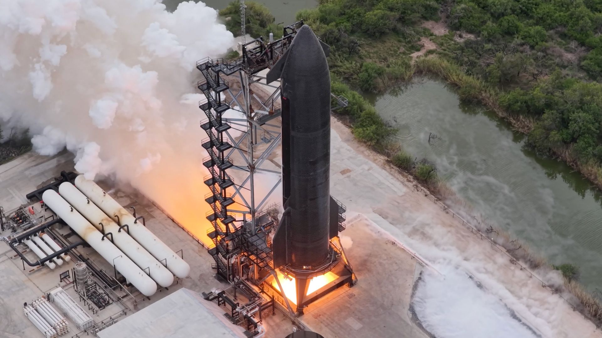 aerial drone photo of a tall black rocket firing its engines on a test stand