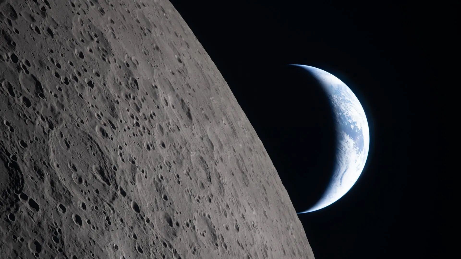 photo from a spacecraft flying around the moon, showing a crescent earth beyond the lunar limb