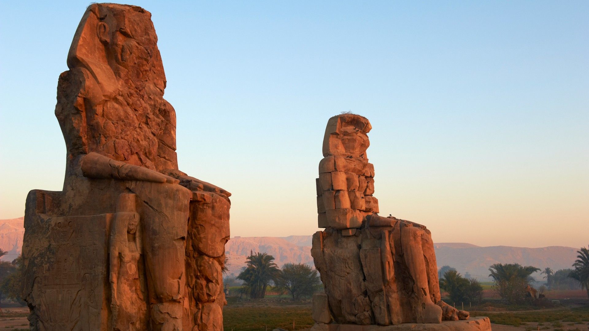 Two giant sitting statues known as the Colossi of Memnon carved to represent the pharaoh Amenhotep III of the dynasty XVIII.
