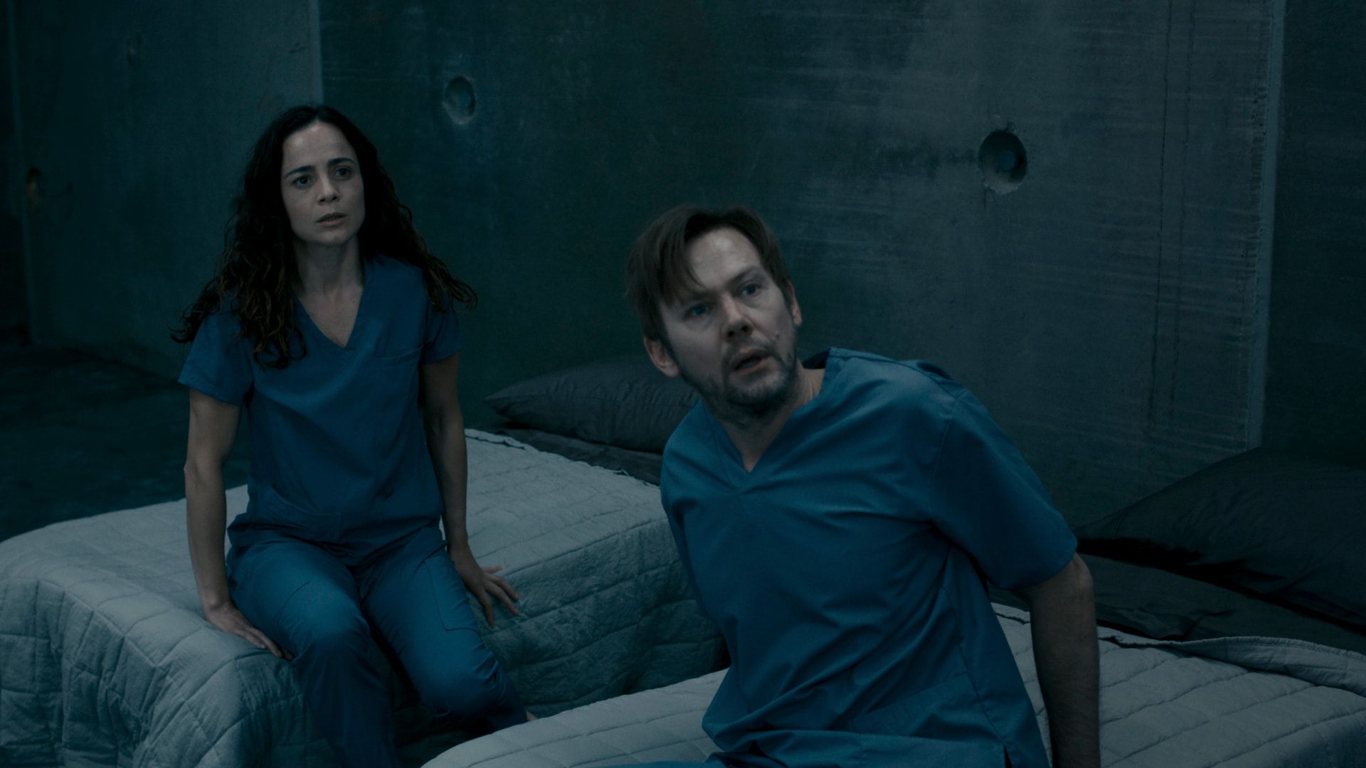 a woman and a man in blue hospital outfits sitting on beds