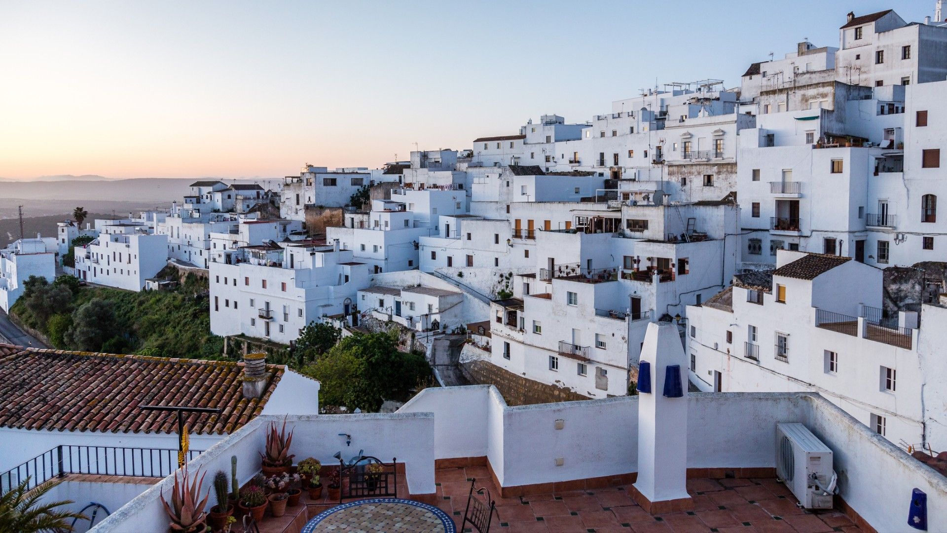 A cluster of whitewashed hillside homes and rooftop terraces at sunset, creating a peaceful view of a Mediterranean village.