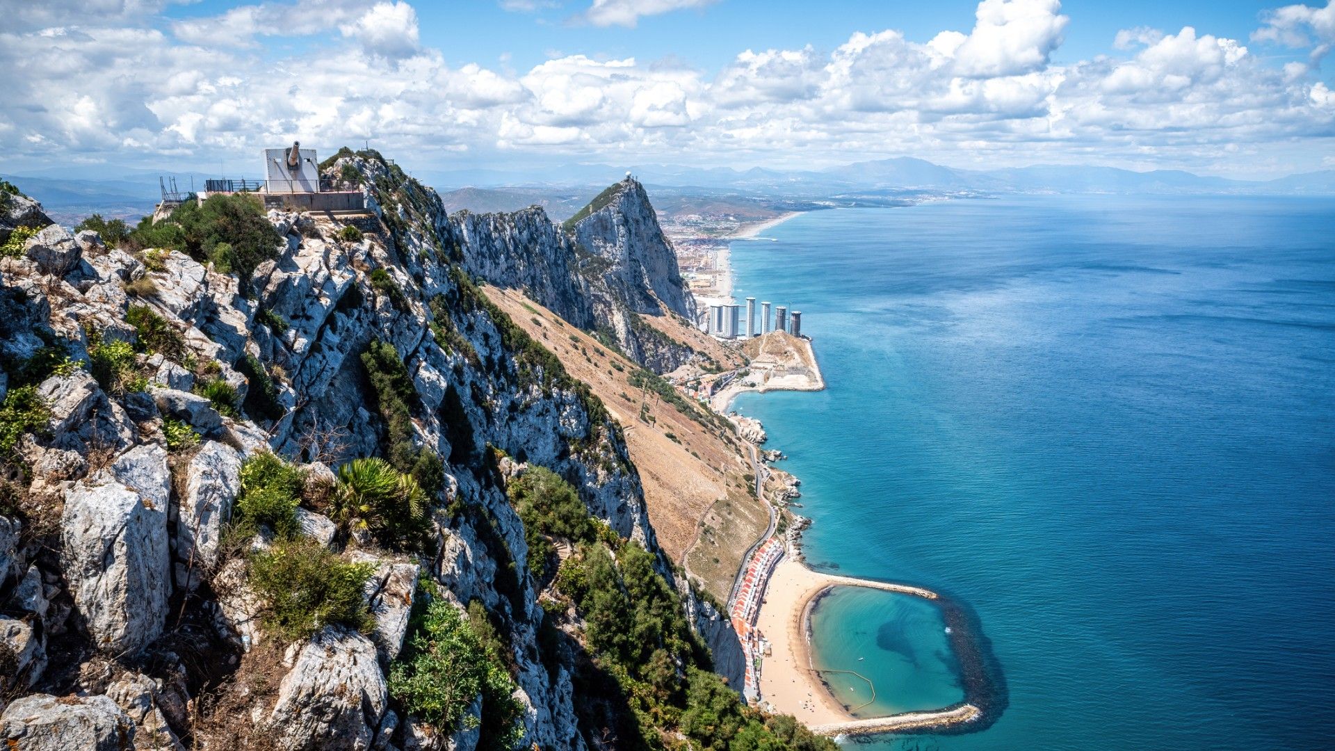 Breathtaking aerial view of Gibraltar, showcasing the iconic Rock, the city nestled below, the vast expanse of the sea, and the distant African coast under a picturesque cloudy sky.