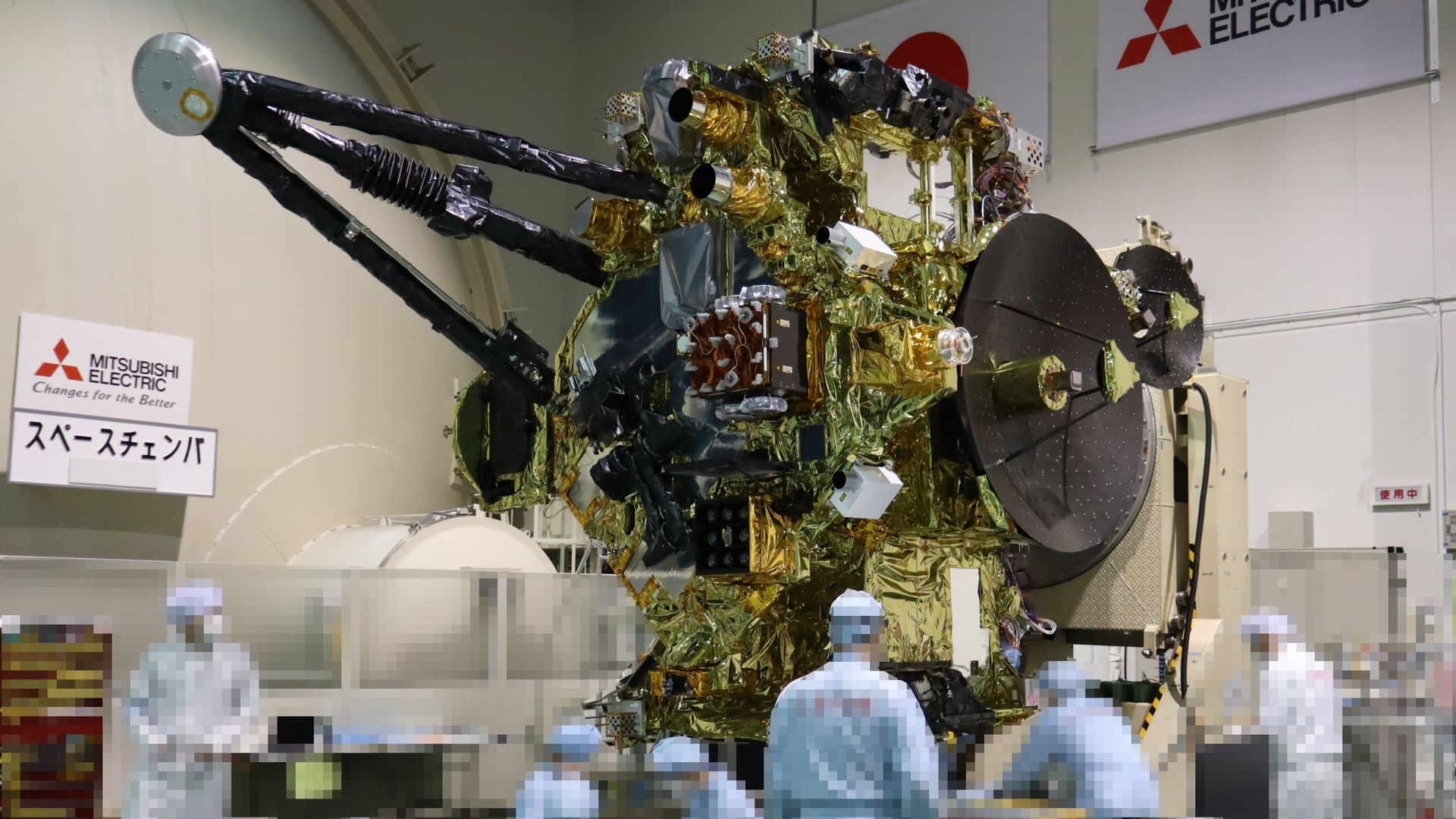 a handful of technicians work with a large spacecraft in a cleanroom