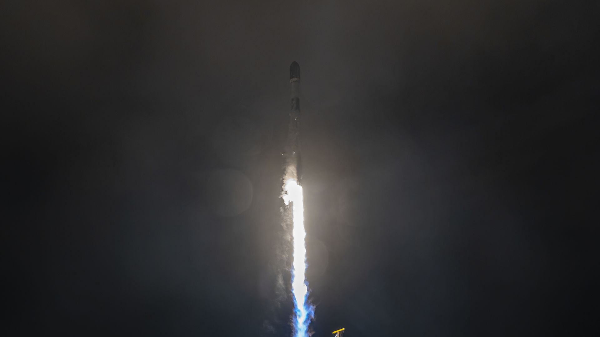 A white rocket blasts off in the dark of night.